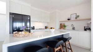 A modern kitchen with a large island, white cabinetry, and a black refrigerator. - Hilltop Haven – breathtaking ocean and mountain panoramas (Kiama)