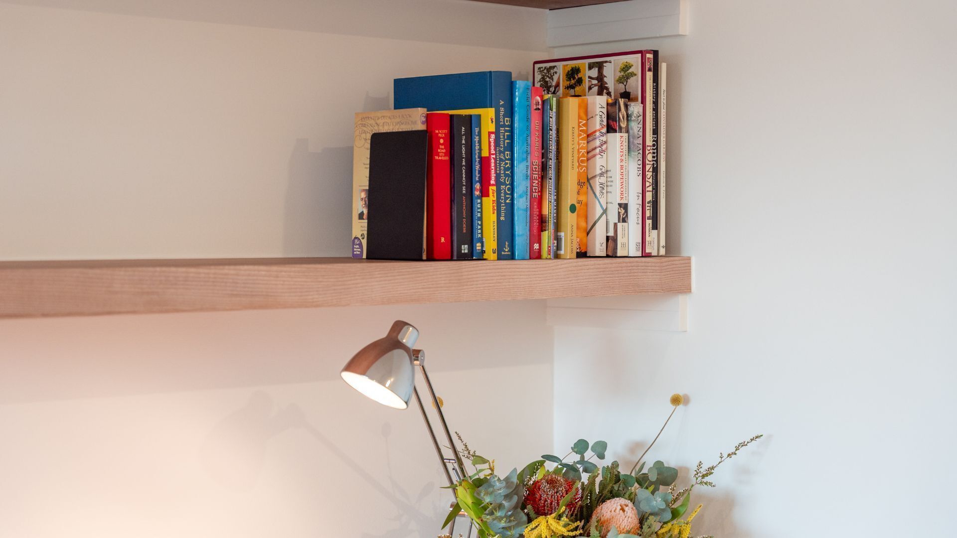 Uma estante com vários livros e uma pequena luminária de mesa.
