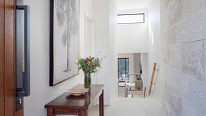 A hallway with a wooden table, a vase with flowers, and a framed artwork on the wall. - Hilltop Haven – breathtaking ocean and mountain panoramas (Kiama)