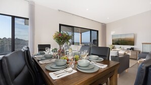 A dining area with a wooden table set for four, large windows, and a view of the landscape. - Hilltop Haven – breathtaking ocean and mountain panoramas (Kiama)