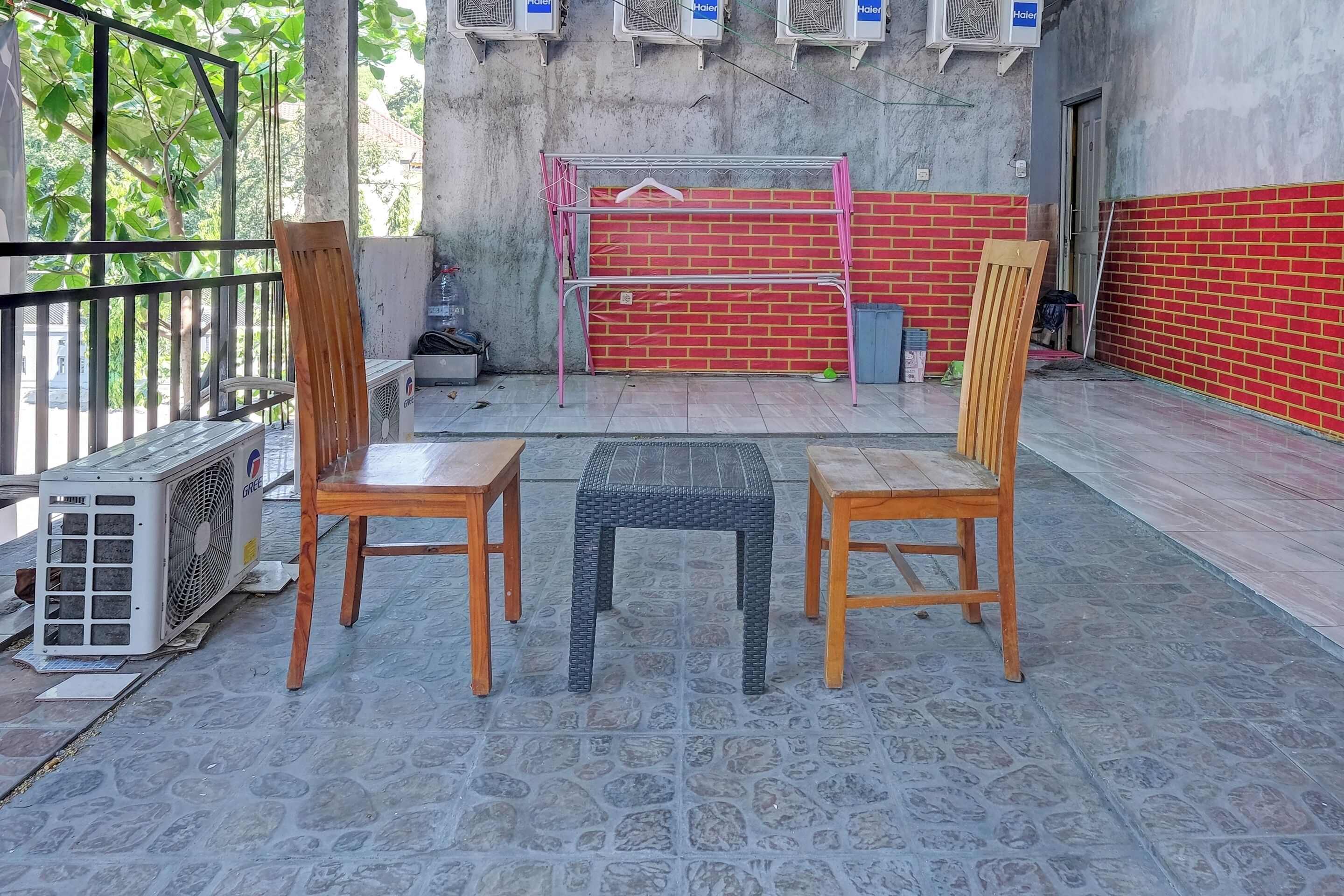 A terrace with two wooden chairs and a small table, a metal bench, and an air conditioning unit.