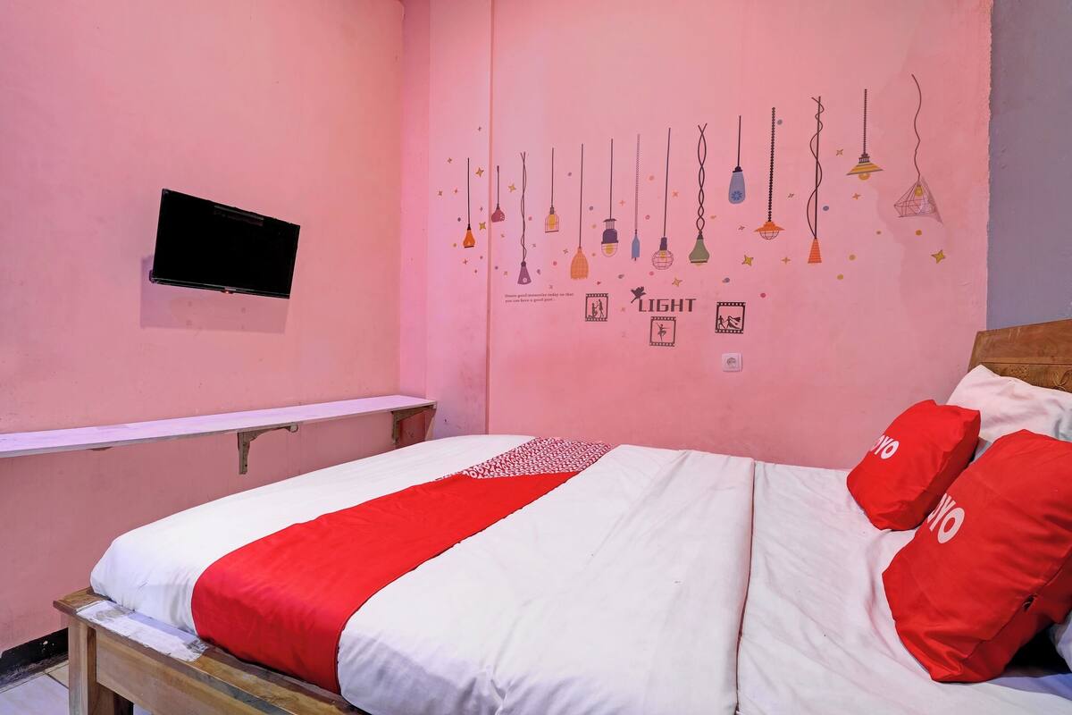 Ein Schlafzimmer mit einem Bett, einem an der Wand montierten Fernseher und einer Wanddekoration aus hängenden Glühbirnen.