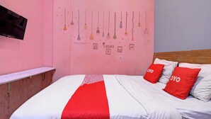 A bedroom with a pink wall, a bed with white and red bedding, and a wall-mounted TV. - OYO Life 92877 Hotel Rainbow 7296 (Semarang)