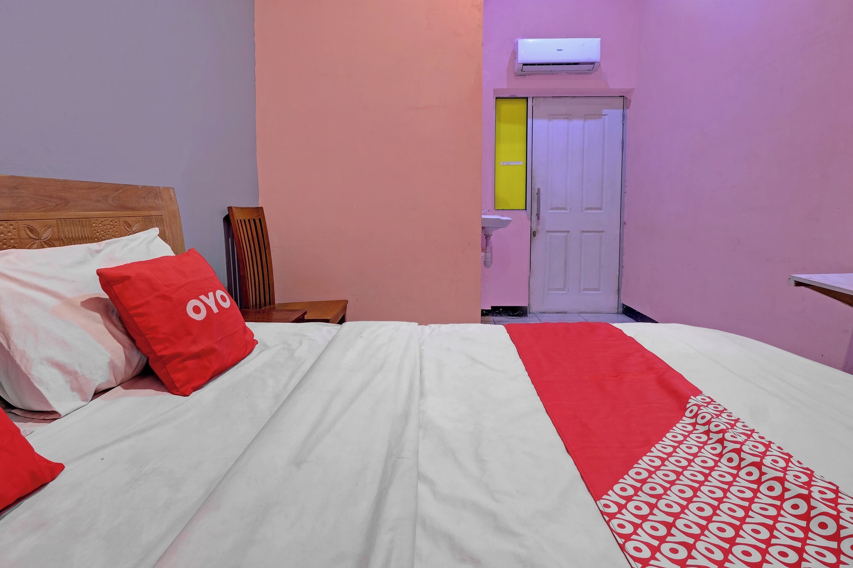 Ein Hotelzimmer mit einem Bett, Kissen, einem Nachttisch, einem Sessel, einem Waschbecken und einer Klimaanlage.