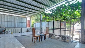 An outdoor covered area with tiled flooring, two wooden chairs, a table, and two air conditioning units. - OYO Life 92877 Hotel Rainbow 7296 (Semarang)