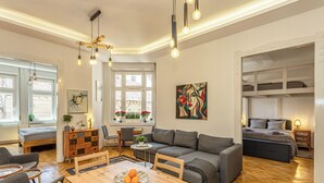 Uma sala de estar moderna com uma mesa de jantar de madeira, sofá cinza e uma cama com cabeceira.