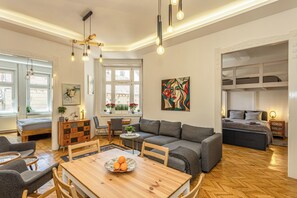 A modern living room with a wooden dining table, grey sofa, and a bed with a headboard.