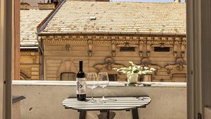 A balcony with a table, a bottle of wine, and glasses, overlooking a building with a tiled roof.