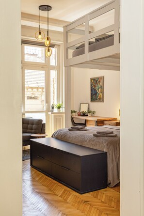 A bedroom with a bunk bed, a desk, a chair, a bench, and a painting on the wall.