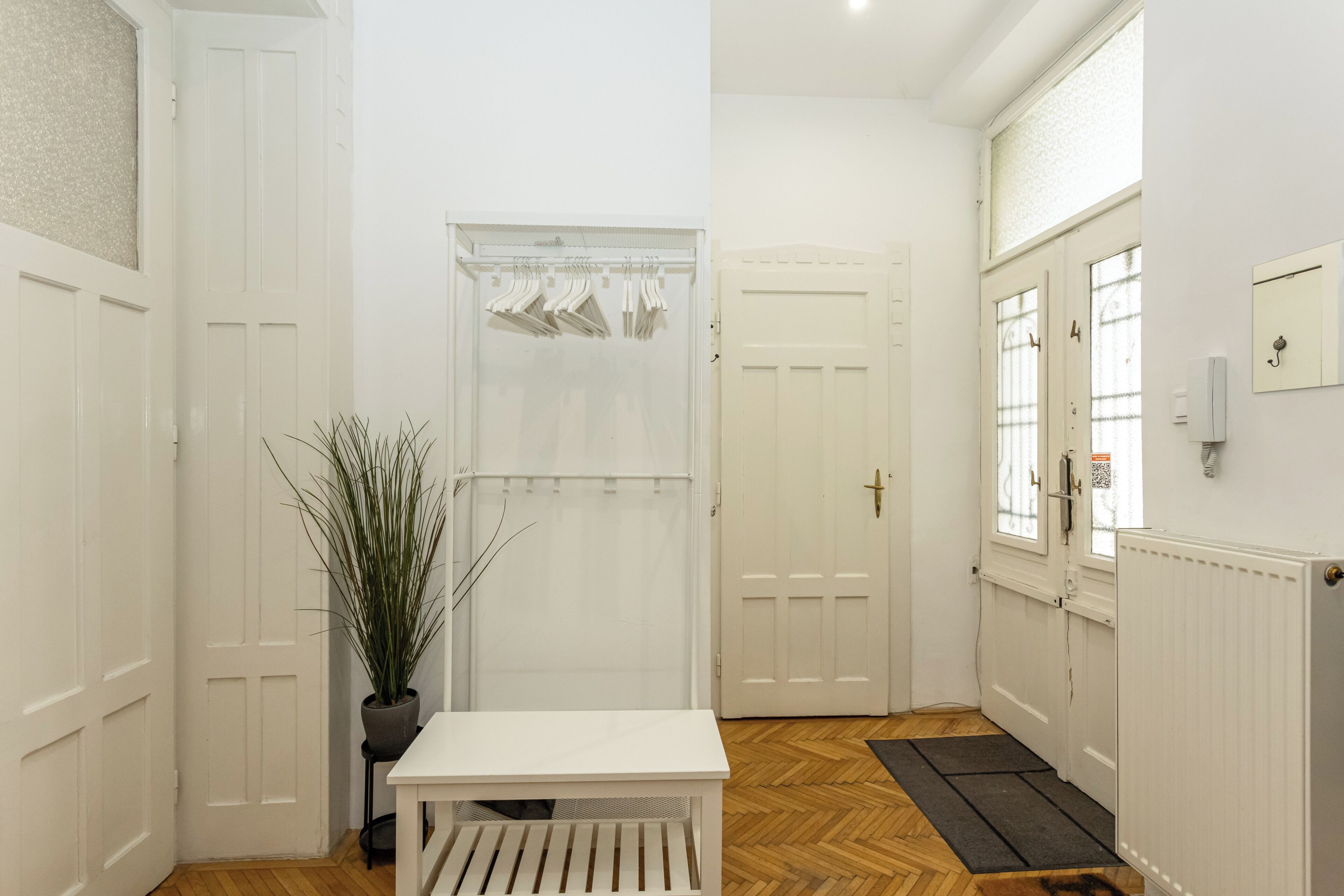 A hallway with white doors, a potted plant, a white bench, and a radiator.