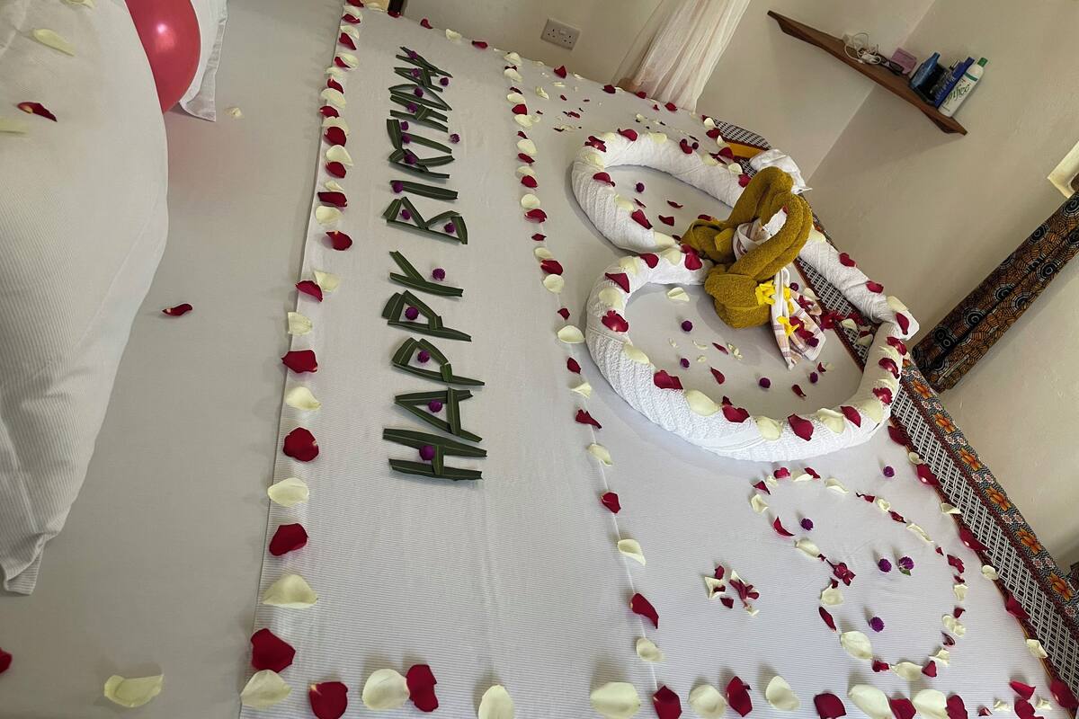 A bed with a white sheet, a red balloon, and a 'Happy Birthday' decoration.