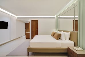 A modern hotel room with a large bed, a bedside table, a mirror, and a flat-screen TV mounted on the wall.