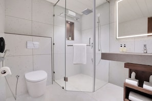 A modern bathroom with a glass-enclosed shower, a white toilet, and a wooden vanity with a mirror.