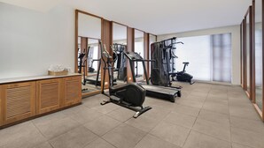 Un gimnasio con máquinas de cardio, una cinta de correr y un espejo grande.