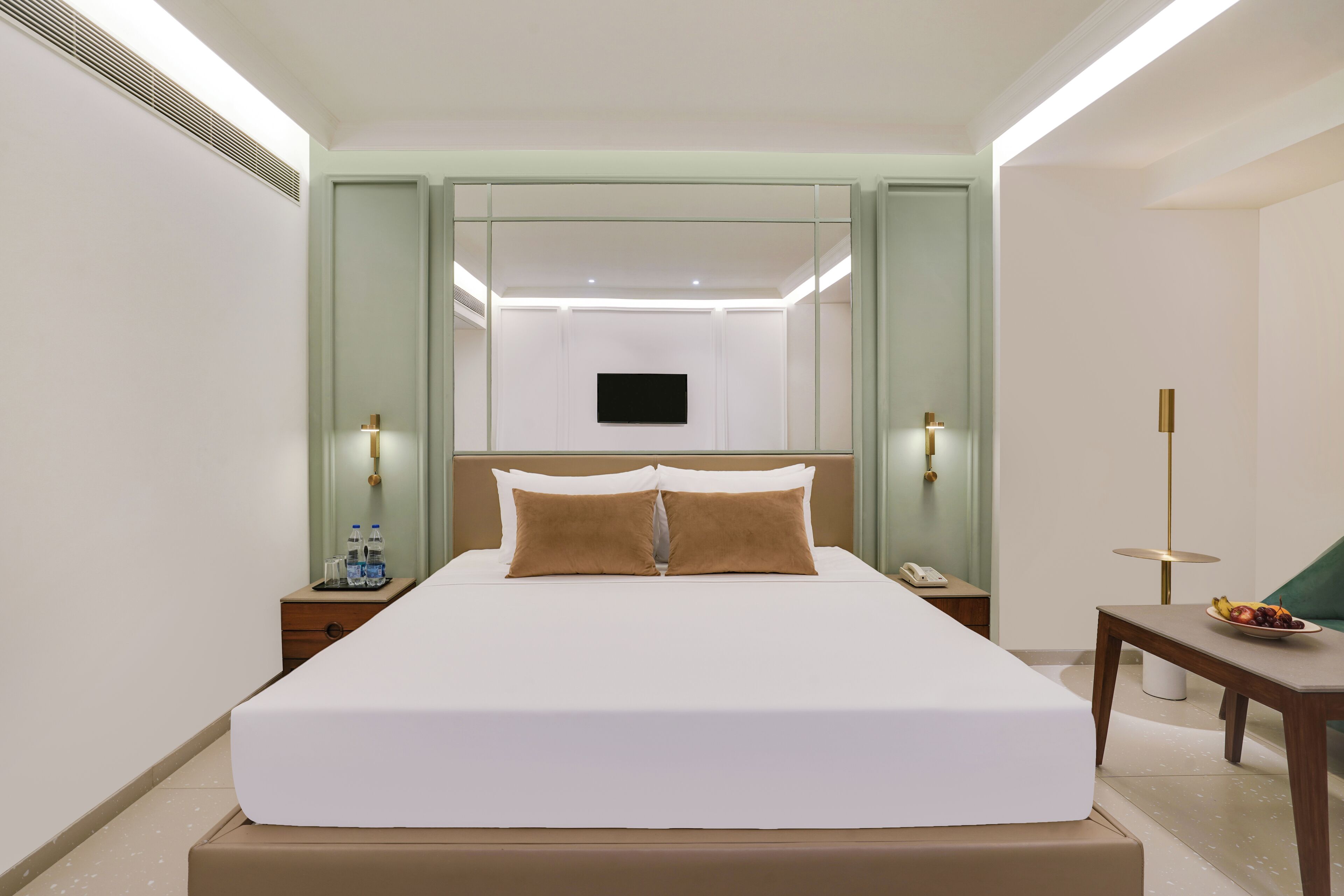 A hotel room with a large bed, bedside tables, a flat-screen TV, and a small table with fruit.