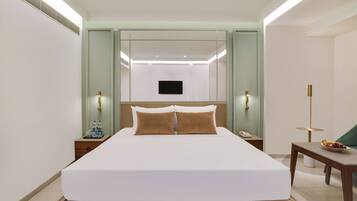 A hotel room with a large bed, bedside tables, a flat-screen TV, and a small table with fruit.