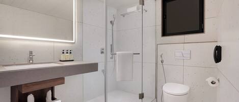 A modern bathroom with a glass-enclosed shower, a large mirror, a toilet, and a wooden shelf with towels.