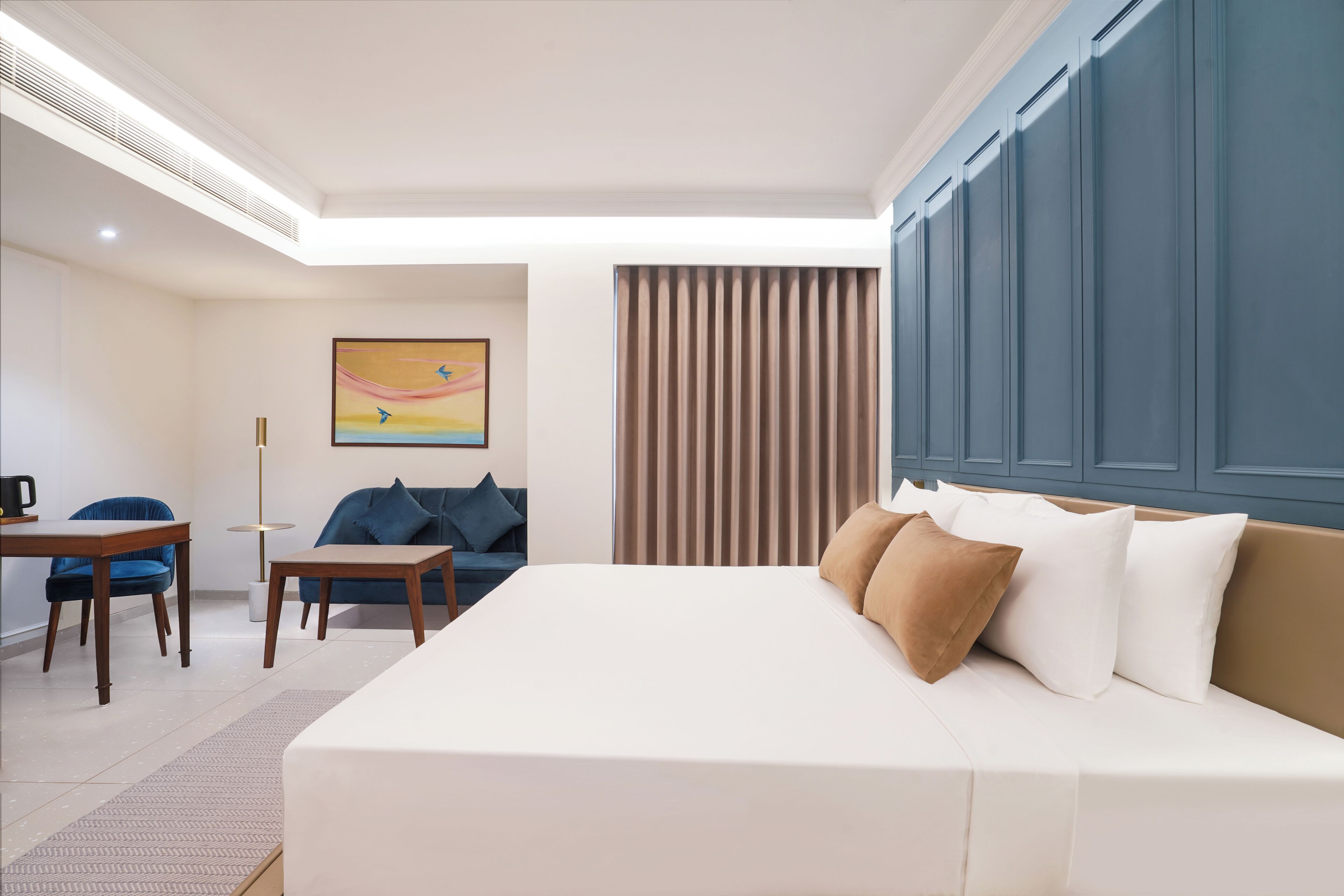 A hotel room with a large bed, a desk, a chair, a sofa, and a painting on the wall.