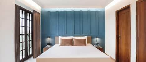A neatly arranged bedroom with a large bed, a nightstand, a window with curtains, and a blue accent wall.