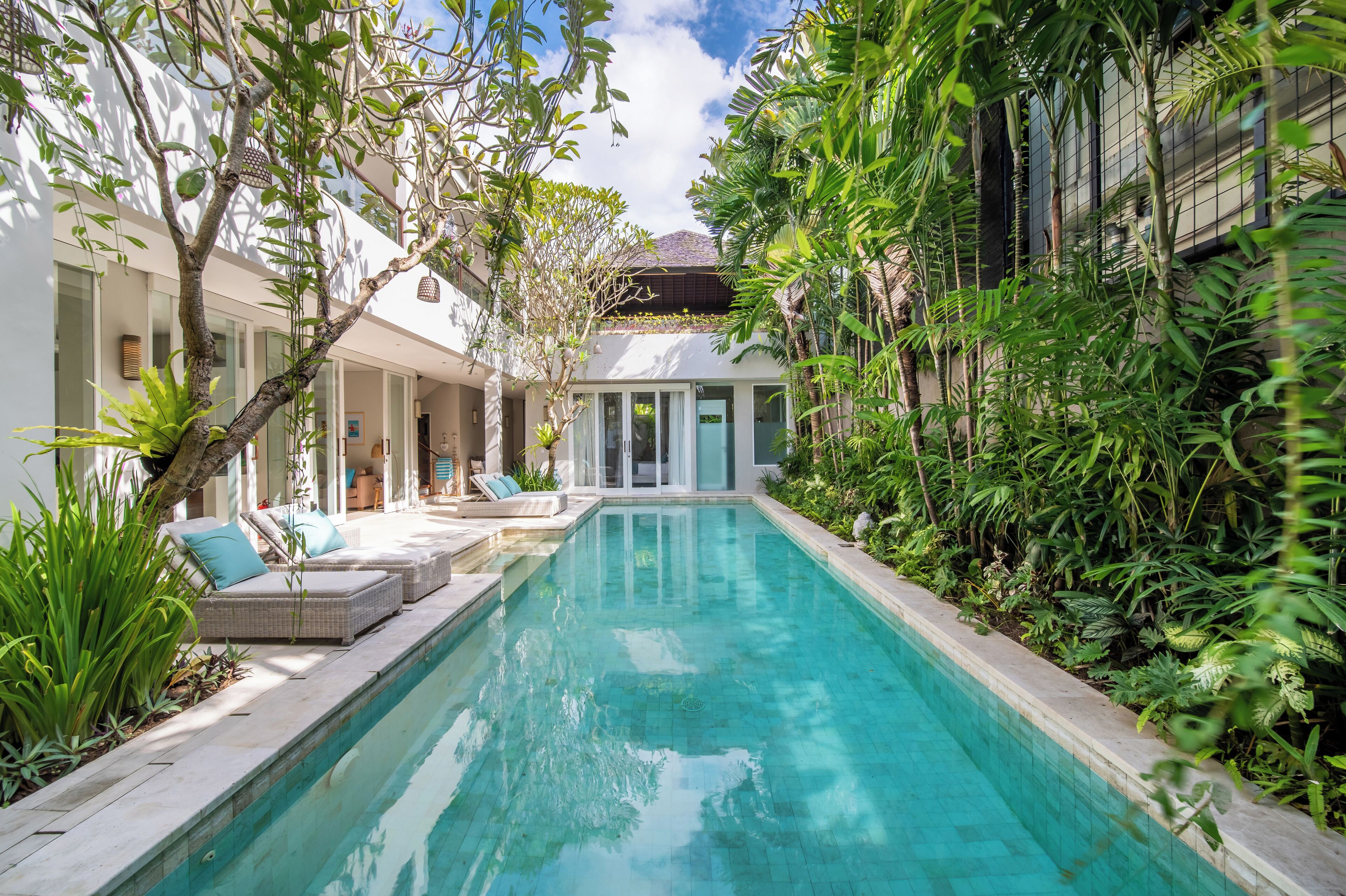 Ein Pool mit Liegestühlen und einer überdachten Liegefläche, umgeben von üppiger Vegetation und moderner Architektur.