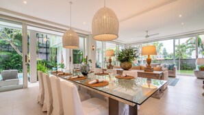 A spacious dining area with a glass table, white chairs, and ambient lighting. - Villa Sunsara 4  (Canggu)