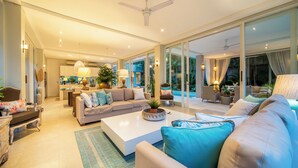 A spacious living room with a large sofa, a coffee table, and a dining area in the background. - Villa Sunsara 4  (Canggu)