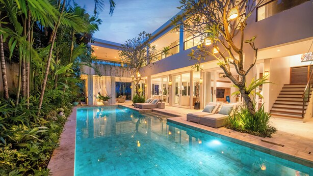 A modern pool area with a clear pool, surrounded by lush greenery and a multi-level building with outdoor seating. - Villa Sunsara 4  (Canggu)