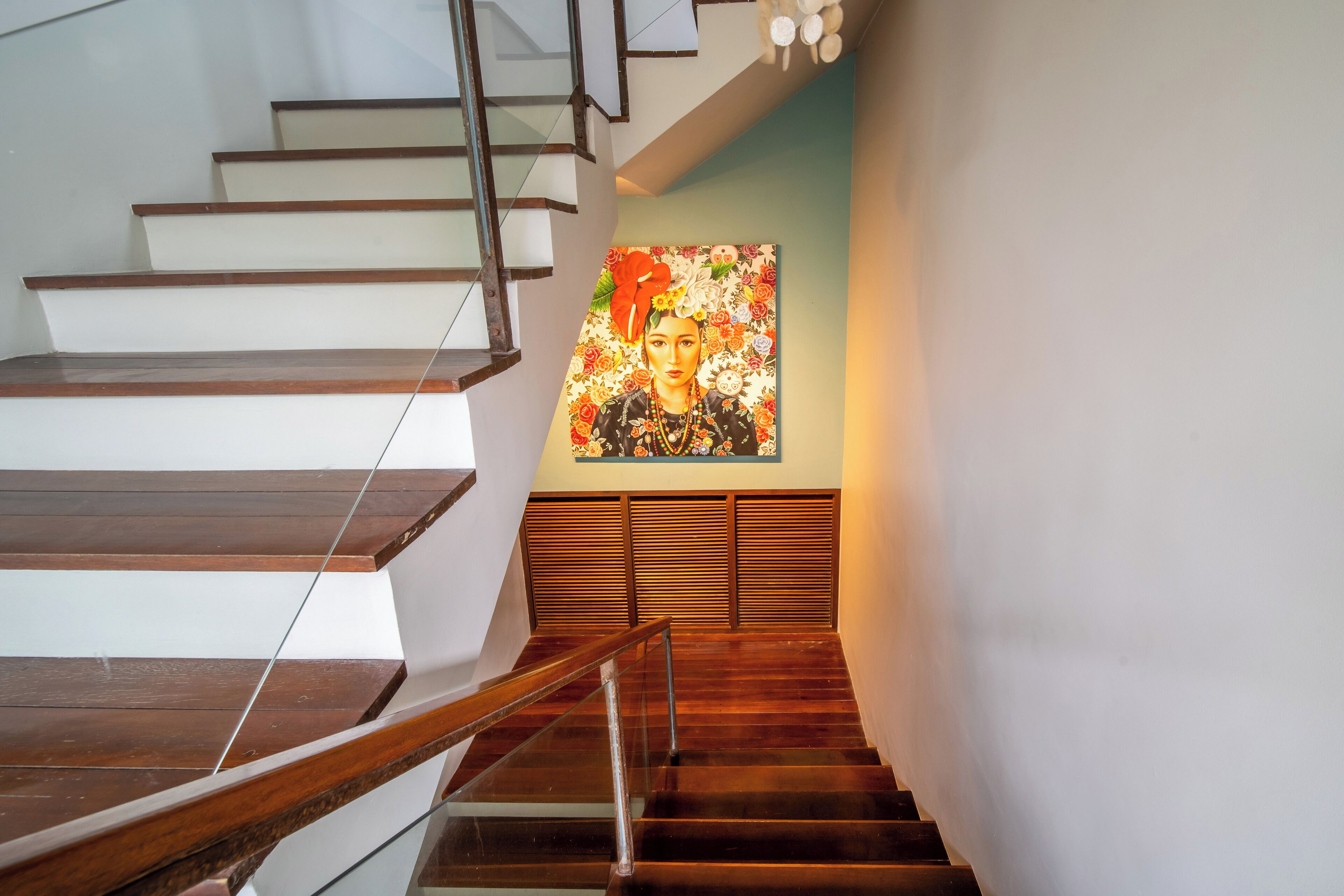 Eine Treppe mit Holzboden und Glasgeländern, die zu einem Raum führt, in dem ein großes Blumenbild an der Wand hängt.