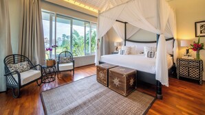 A bedroom with a four-poster bed, a sitting area with chairs, a small table, and a nightstand with a lamp. - Villa Sunsara 4  (Canggu)