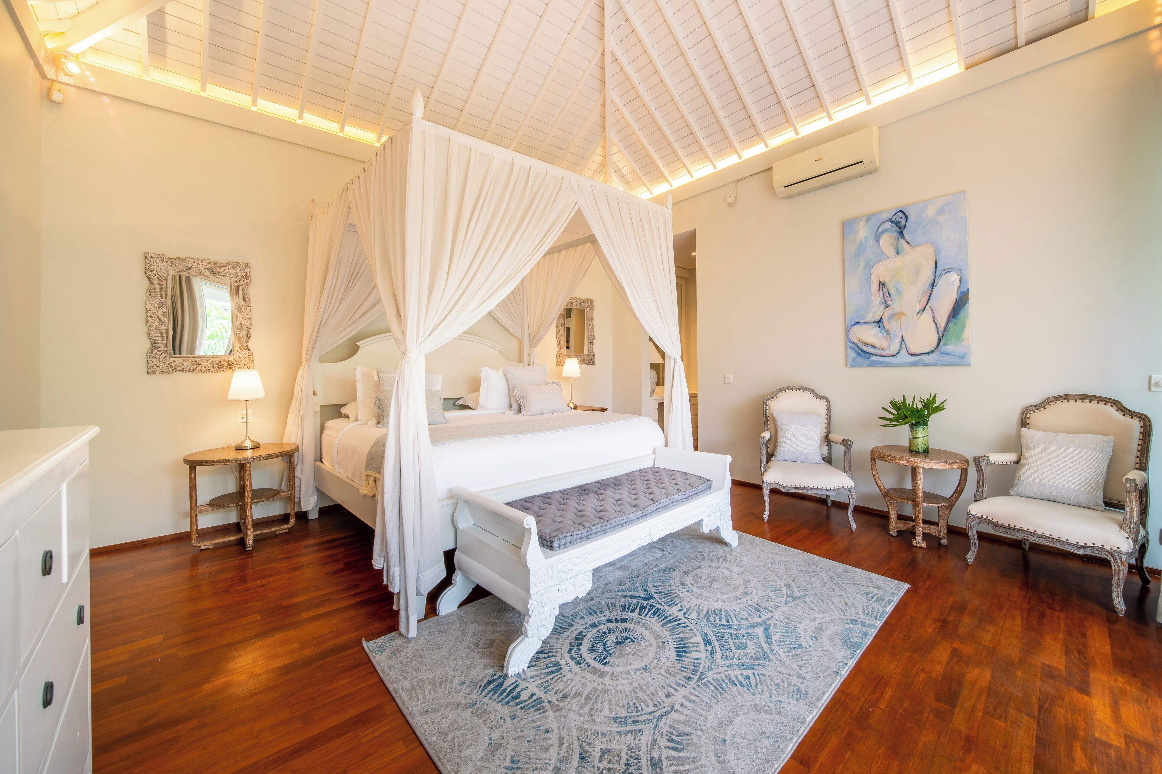 A bedroom with a four-poster bed, a bedside table, a chair, a small table with a plant, and a painting on the wall.