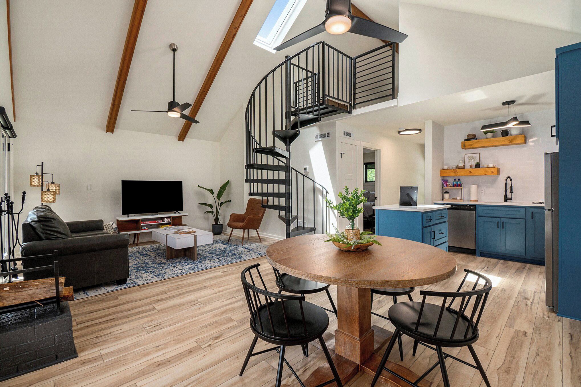 A modern kitchen with blue cabinets, a wooden dining table, and a spiral staircase.