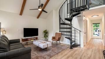 A modern living room with a flat-screen TV, a sofa, a coffee table, and a staircase.