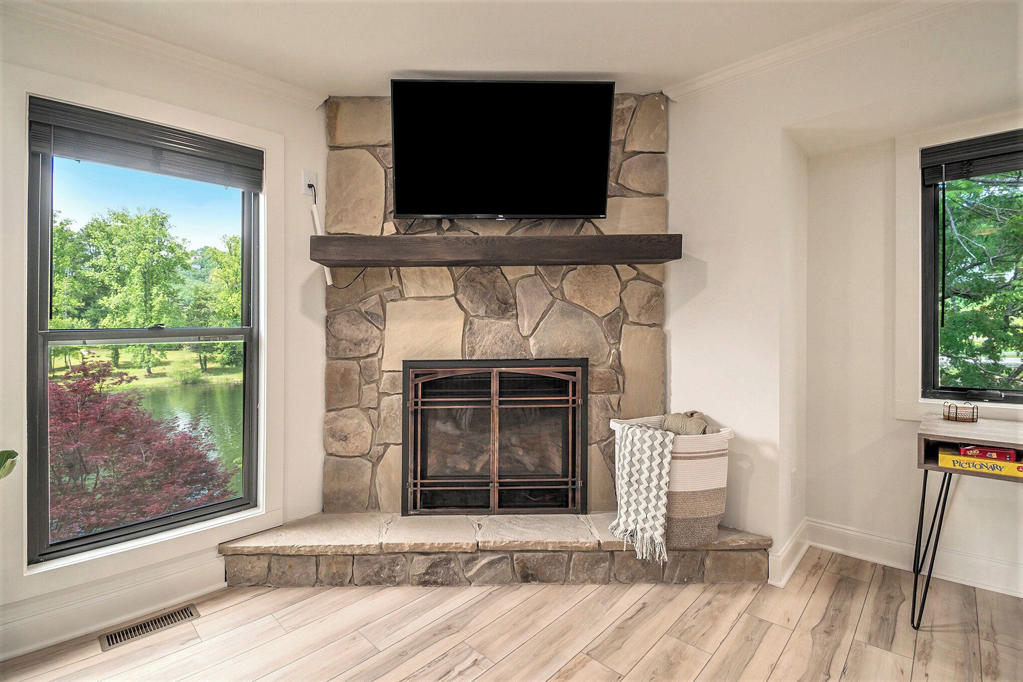 A stone fireplace with a flat-screen TV above it, large windows on either side, and a bench in front.