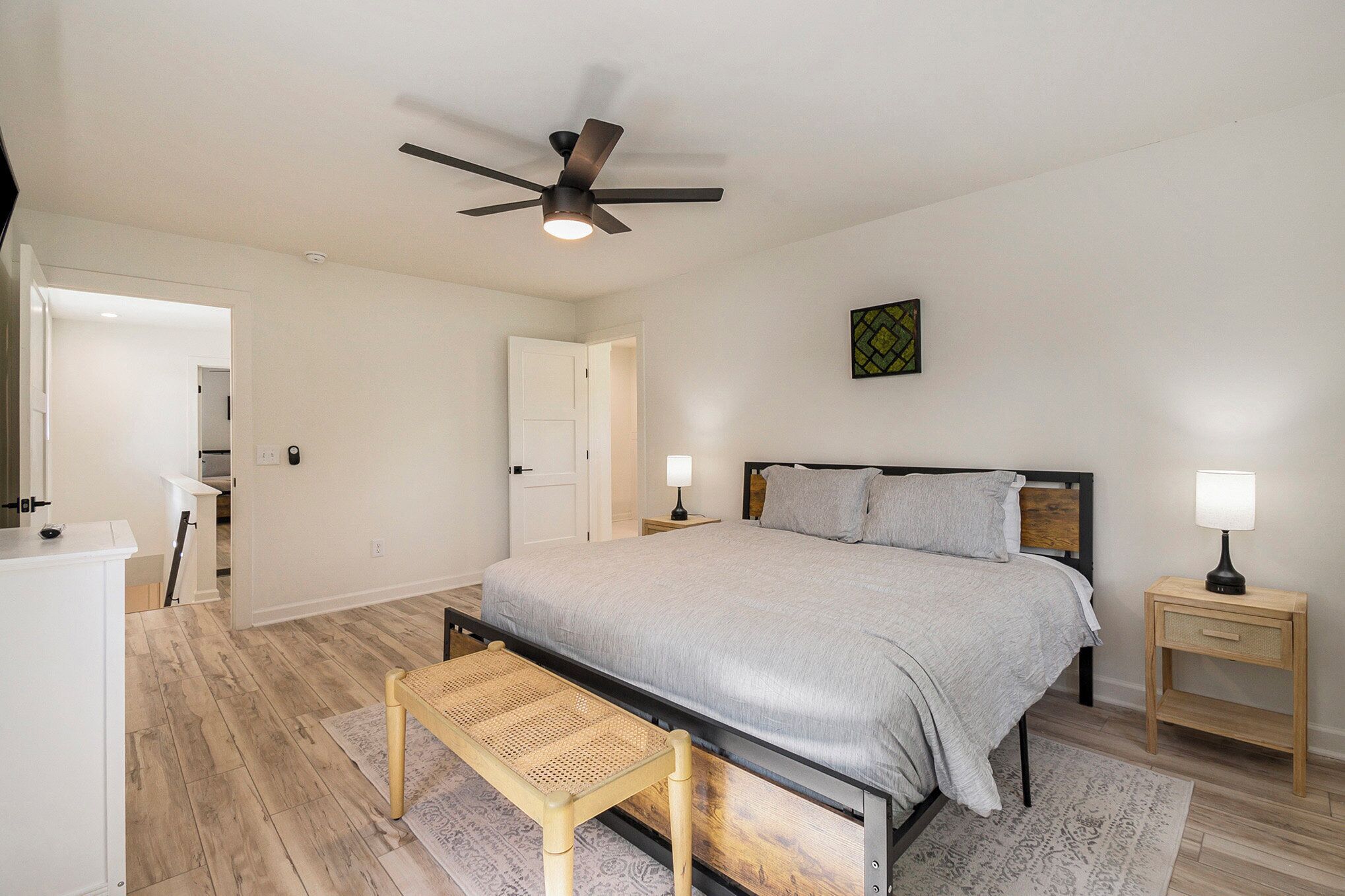 Un dormitorio con cama, mesitas de noche, ventilador de techo y un banco.
