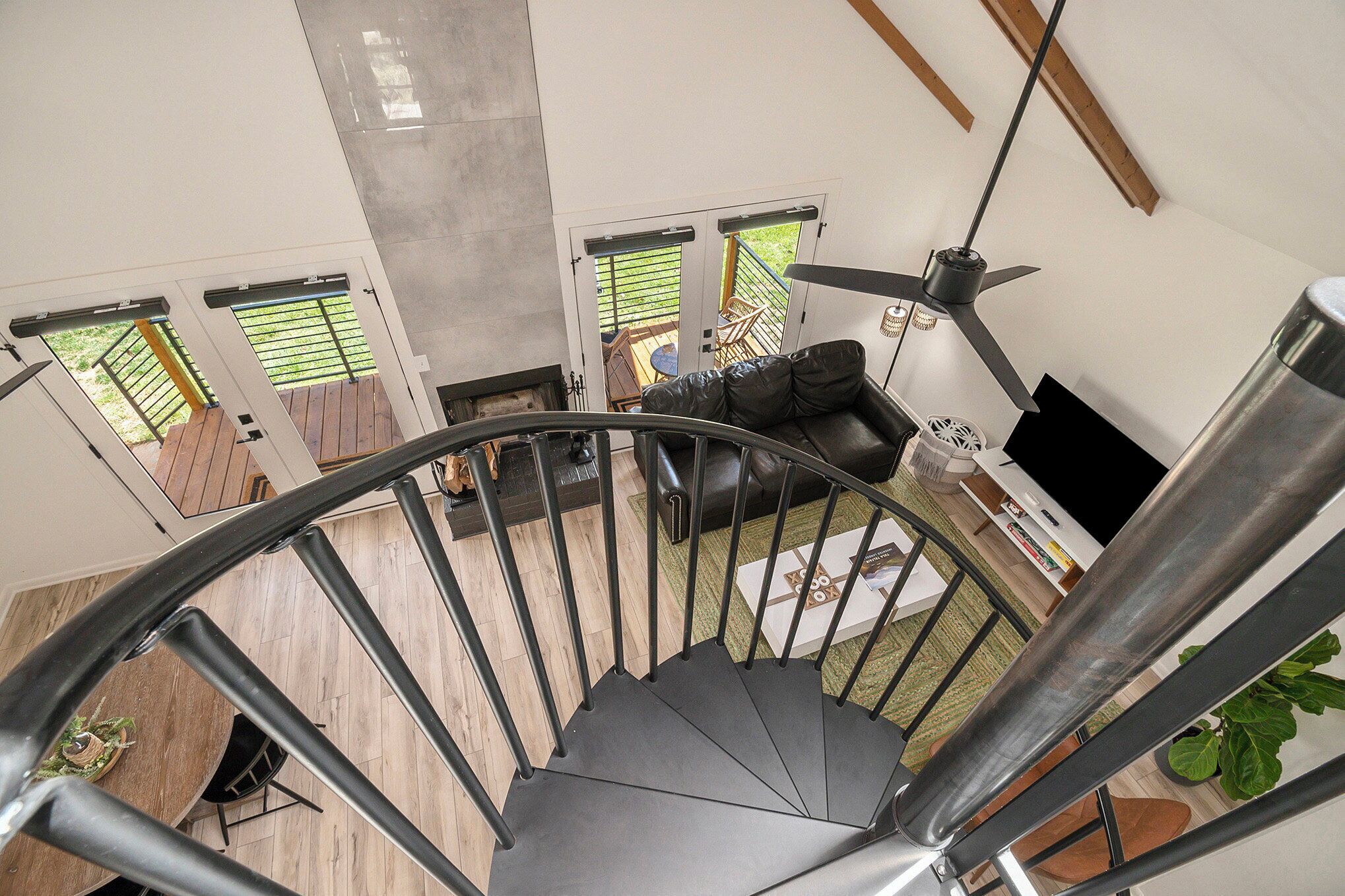 Un interior moderno con una escalera espiral, un sofá de cuero, un televisor y un comedor con mesa y sillas.