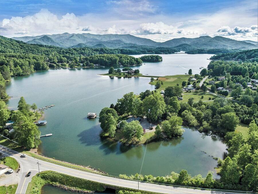 Un lago rodeado de exuberante vegetación y montañas. Hay barcos amarrados cerca de la orilla, y una carretera corre a lo largo de la orilla del lago.