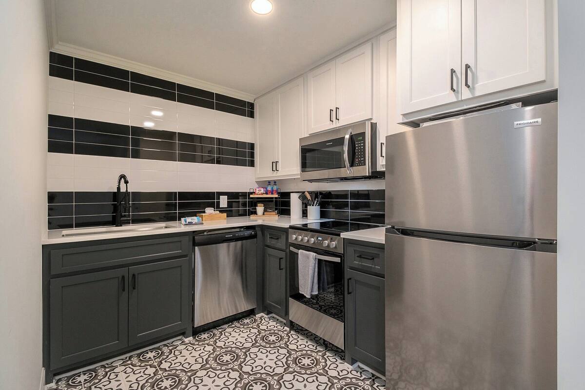 Uma cozinha moderna com eletrodomésticos de aço inoxidável, painel de azulejos preto e branco e armários cinzentos escuros.