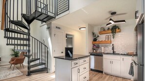 A modern kitchen with a central island, white cabinets, and a black spiral staircase. - Tranquille Resort (Hiawassee)