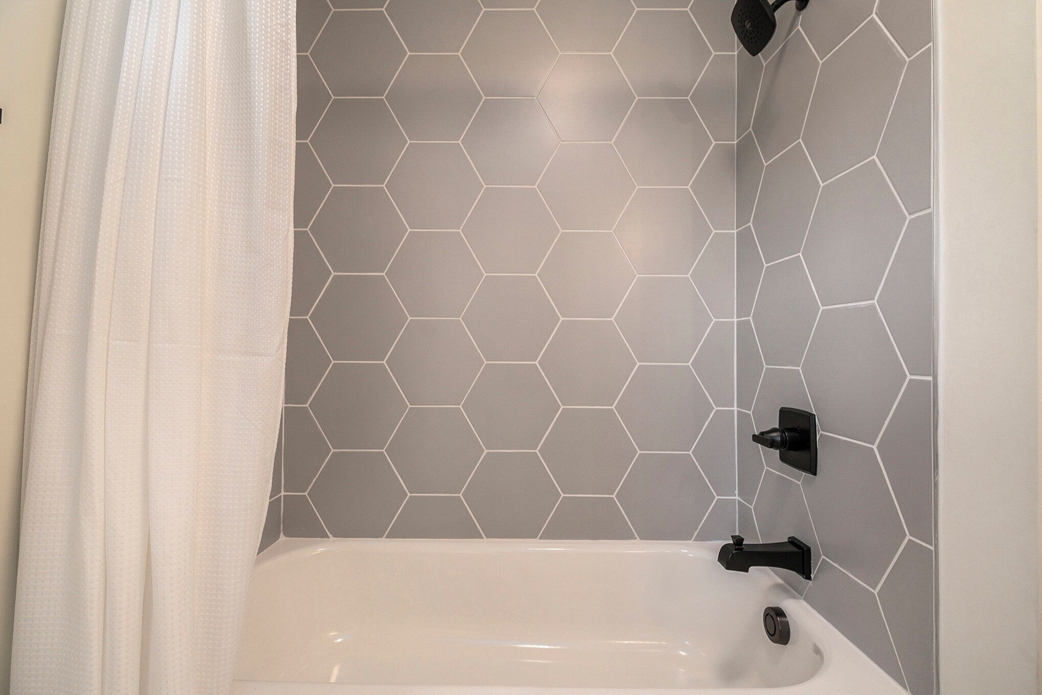 A bathroom with a white bathtub, hexagonal tile backsplash, and black fixtures.