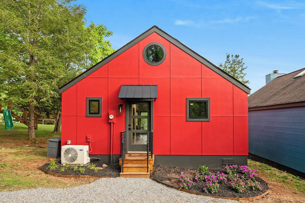 Um edifício vermelho com teto preto, janela circular e um pequeno alpendre.