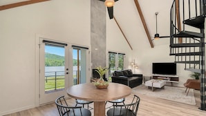 A spacious living area with a dining table, chairs, a sofa, a TV, and a staircase. - Tranquille Resort (Hiawassee)