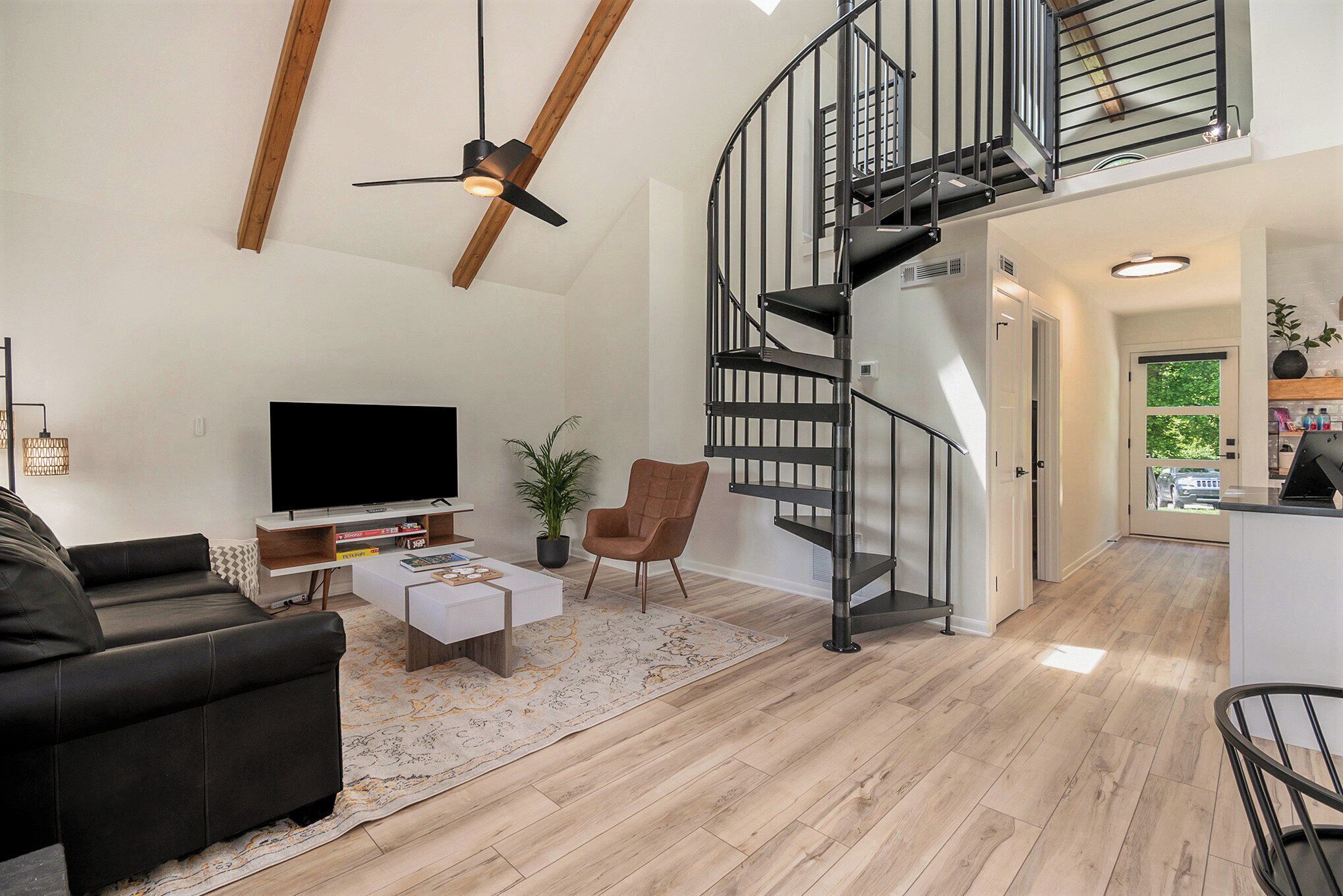 A modern living room with a black leather sofa, a flat-screen TV, a coffee table, and a spiral staircase leading to an upper level.