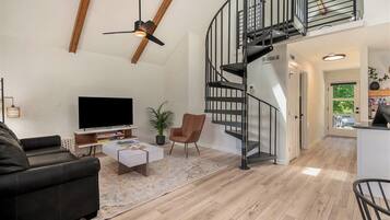 A modern living room with a black leather sofa, a flat-screen TV, a coffee table, and a spiral staircase leading to an upper level.