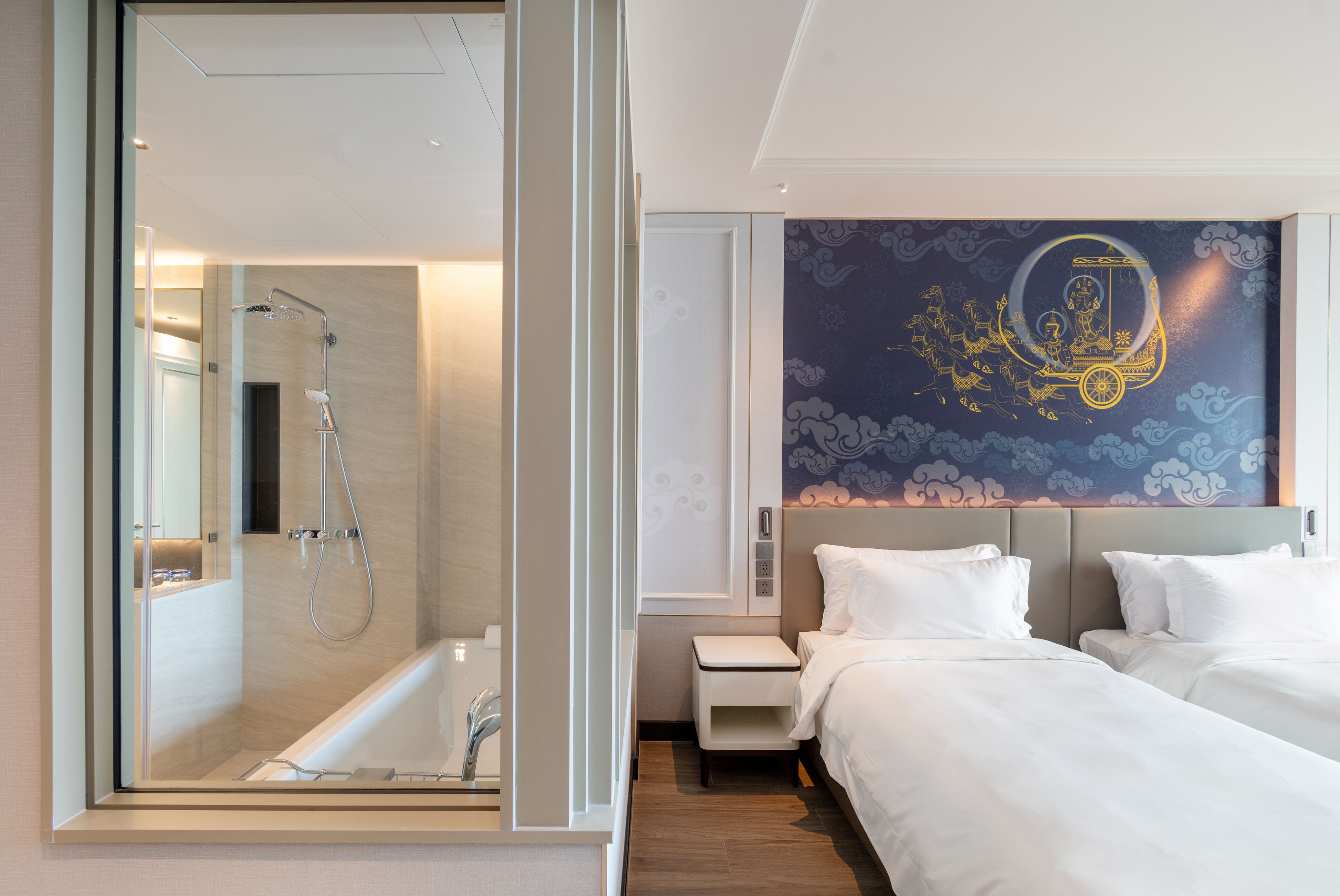 Ett modernt hotellrum med en duschavdelning med glasväggar, en stor säng med vita sängkläder och en dekorativ väggmålning.