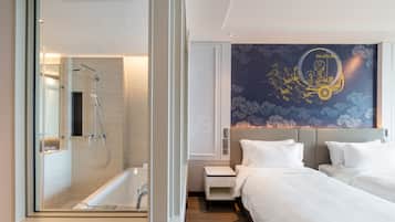 Ett modernt hotellrum med en duschavdelning med glasväggar, en stor säng med vita sängkläder och en dekorativ väggmålning.