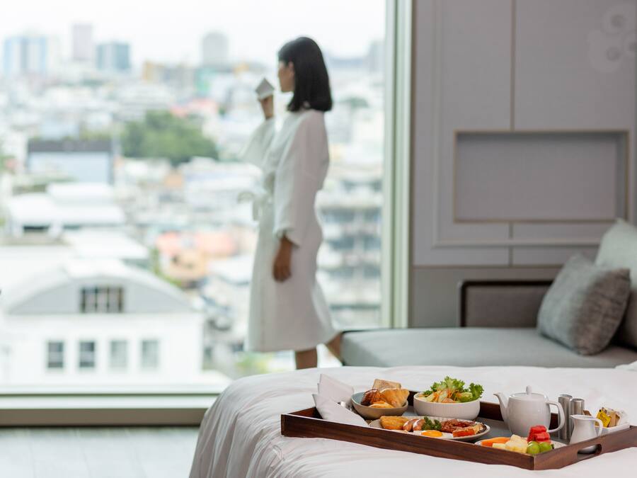 Habitación de hotel con un ventanal grande, cama y una bandeja de desayuno, con vistas a la ciudad.