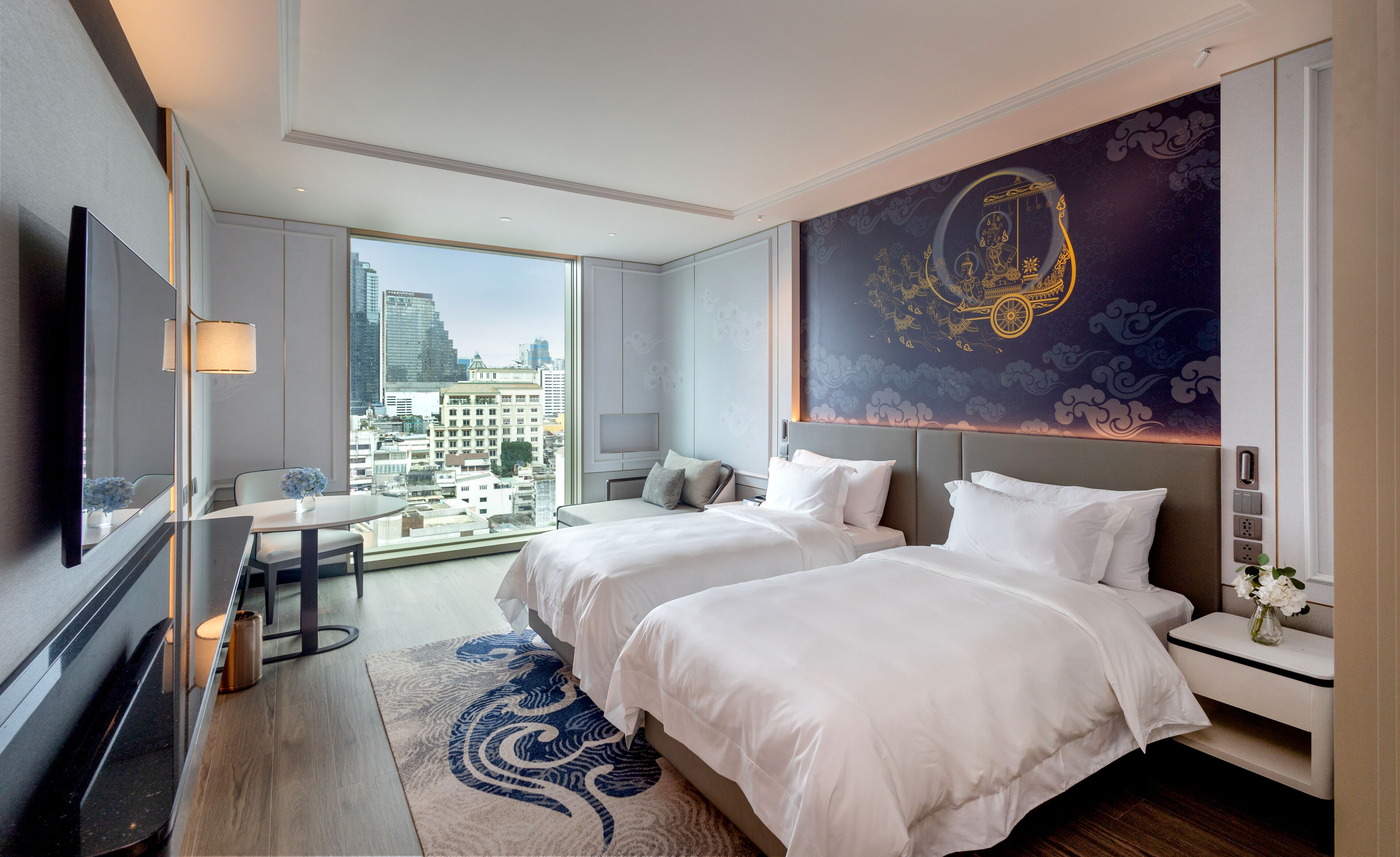 Ein Hotelzimmer mit zwei Betten, einem großen Fenster mit Blick auf die Stadt, einem Flachbildfernseher und einem Wandgemälde.