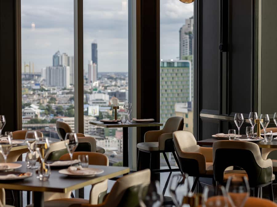 Un restaurant avec des tables dressées pour le service, de grandes fenêtres donnant sur la ville.