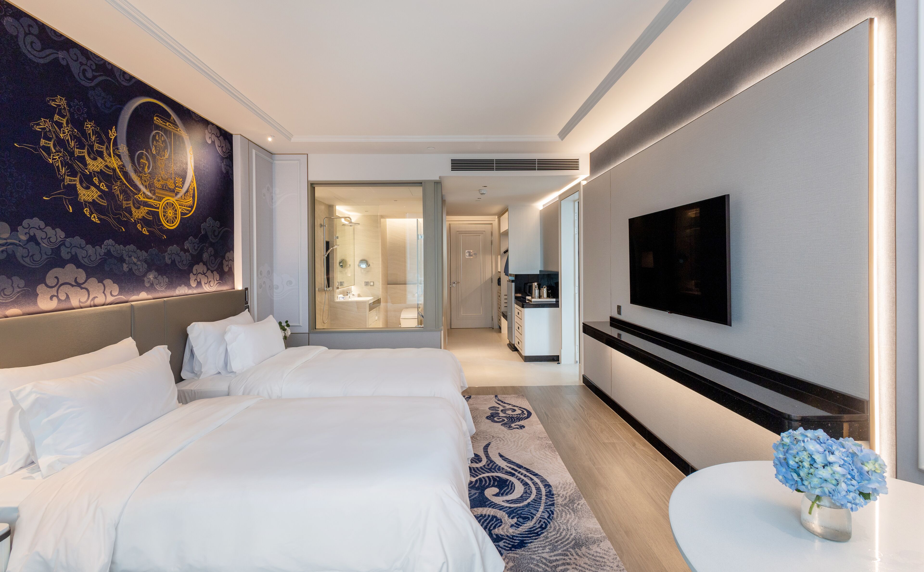 A hotel room with two beds, a TV, a bathroom with a shower, and a decorative wall.