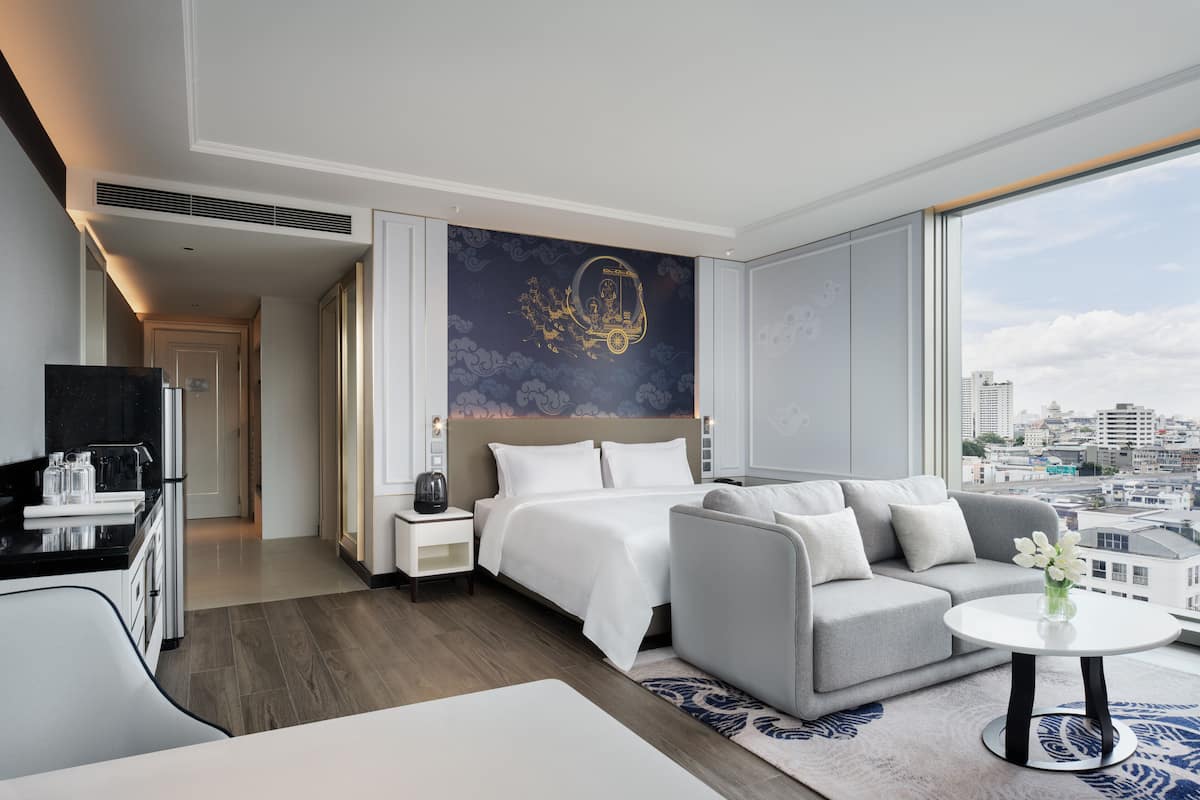 A modern hotel room with a bed, sofa, and a dining area.